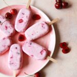 Cherry cheesecake popsicles on a pink plate with fresh cherries