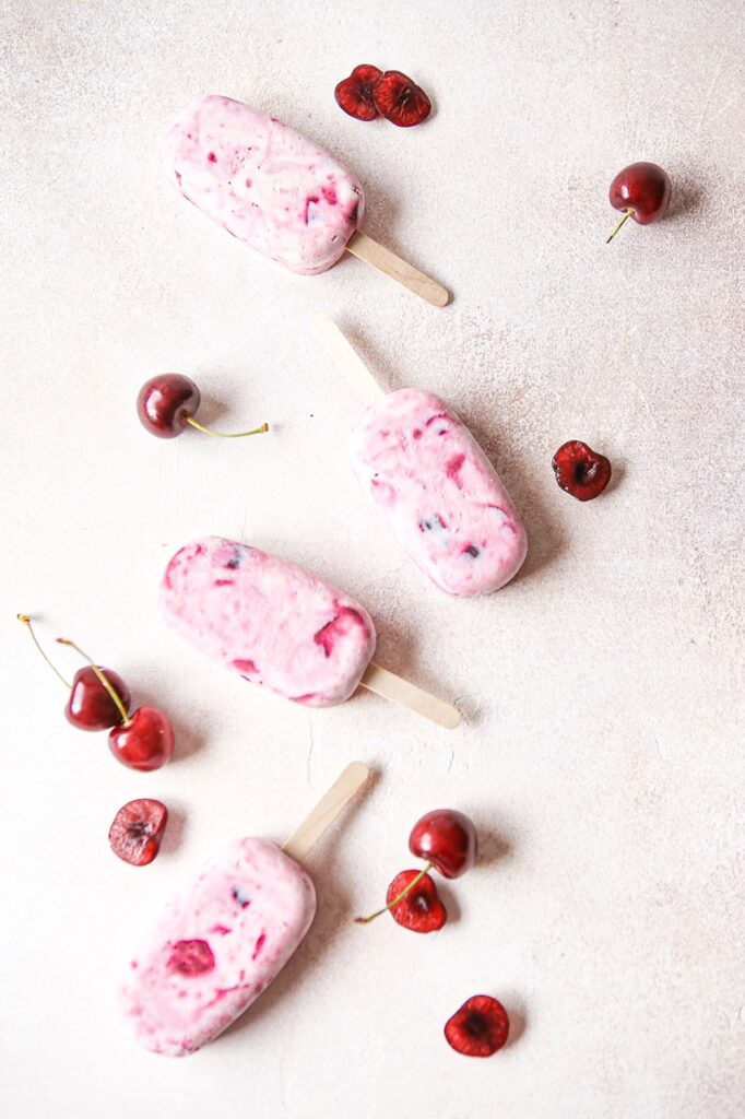 cherry cheesecake popsicles scattered with fresh cherries