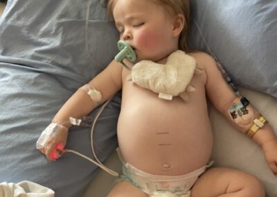 One year old in a hospital bed with an iv and other tubes, sucking on a soother
