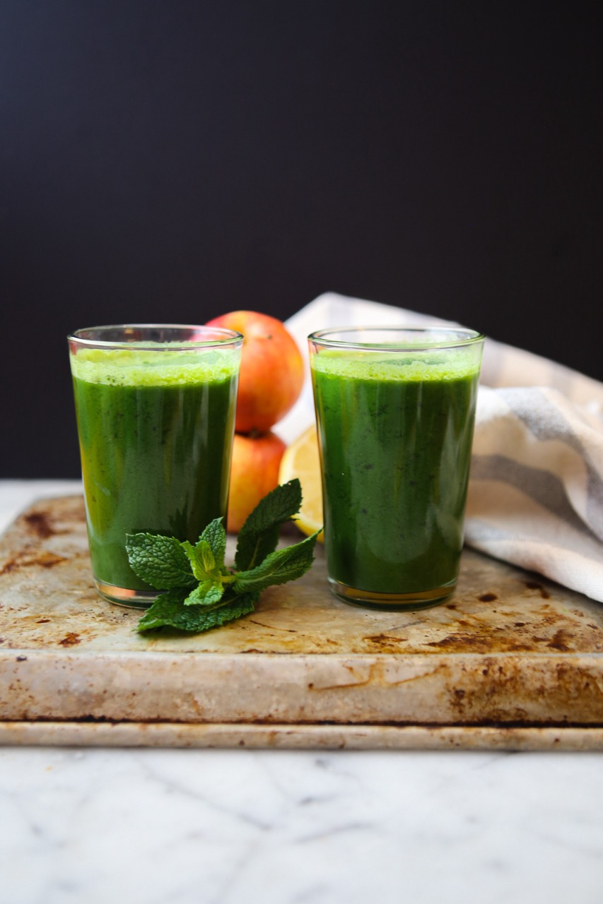 Two tall glasses of vibrant green juice on a tray with fresh mint leaves