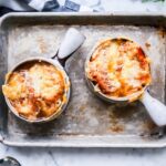 two french onion soups in bowls on a tray with fresh herbs