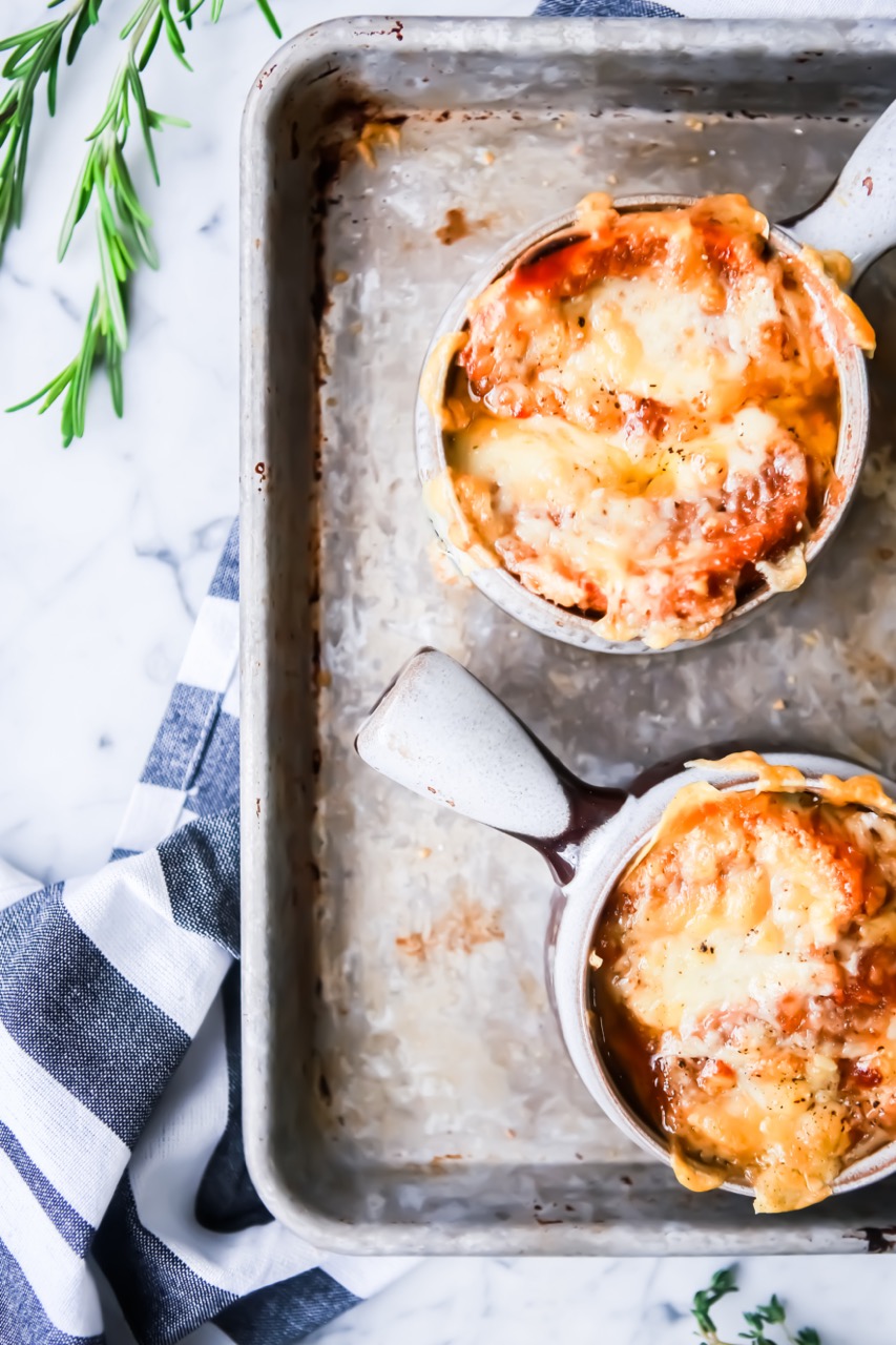 Two french onion soup bowls with fresh herbs on a tray