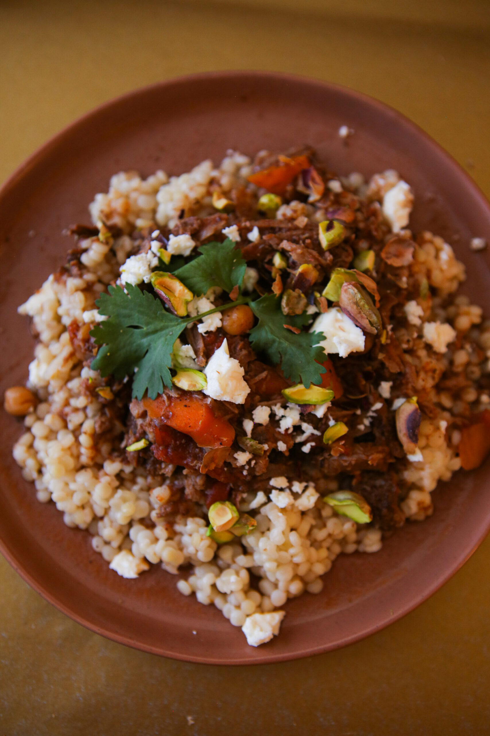 Moroccan beef stew on a plate garnished with pistachios, feta and cilantro