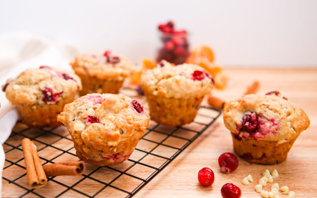 white chocolate cranberry orange muffins on a cooling rack with white chocolate chips and cranberries around it.