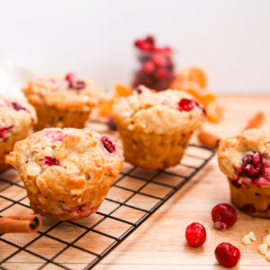 white chocolate cranberry orange muffins on a cooling rack with white chocolate chips and cranberries around it.