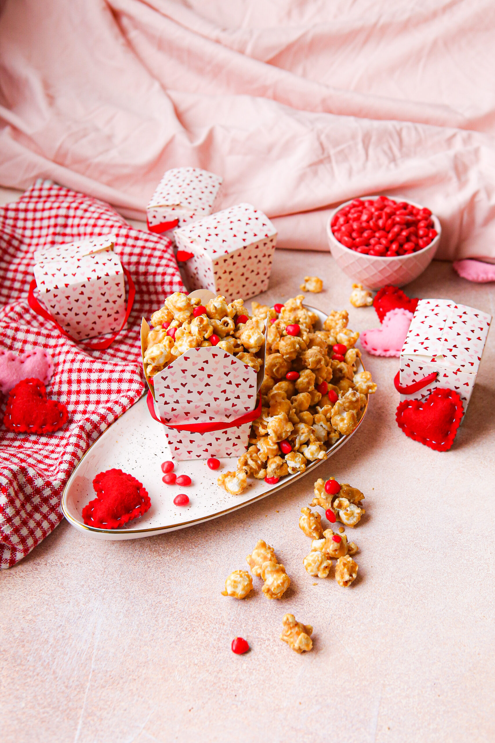Cinnamon heart caramel corn in a box on a little gold rimmed platter with cinnamon hearts around it.