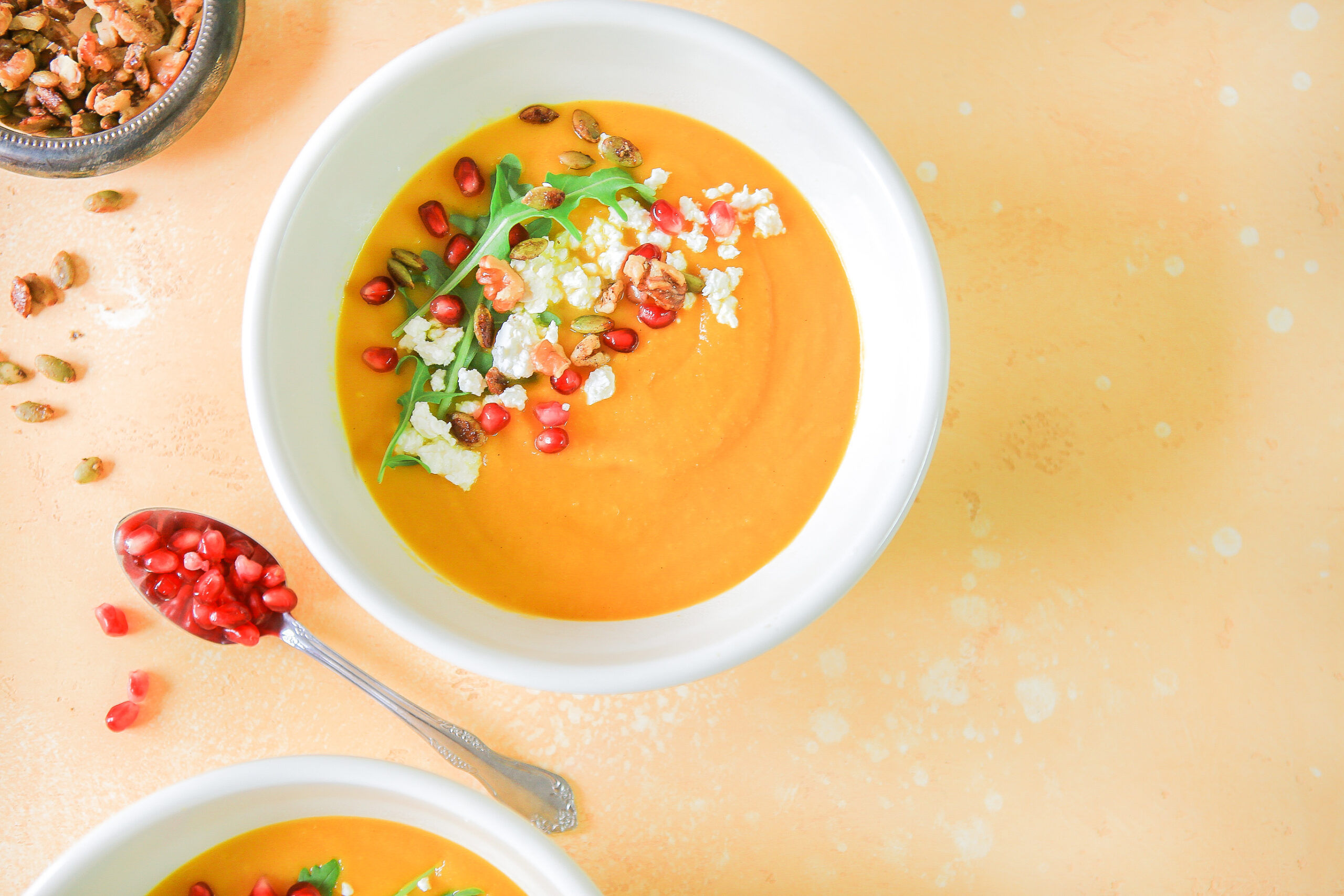 A bowl of butternut squash and apple soup with a spoonful of pomegranate seeds
