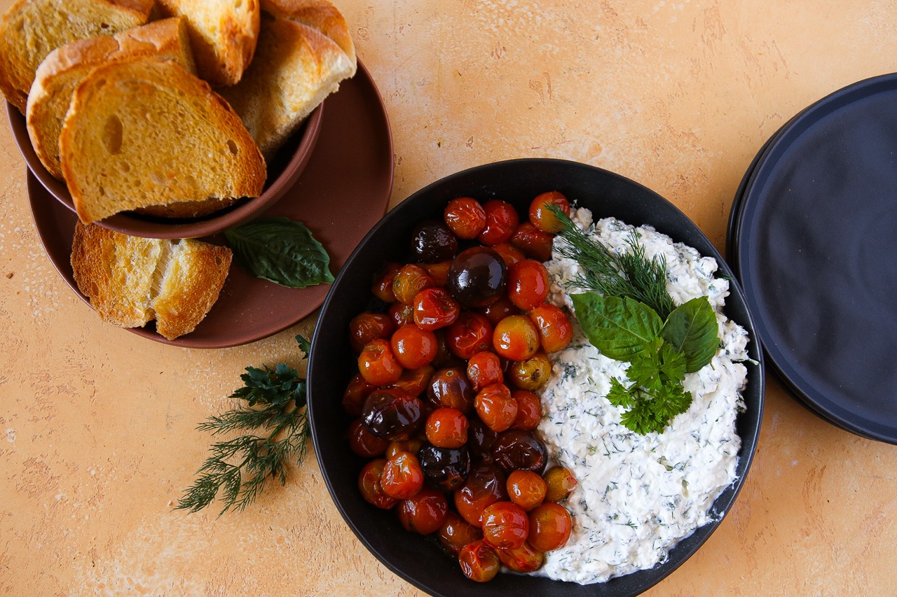 A plate of sourdough crostini next to the whipped feta with herbs and roasted tomatoes